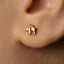 A close-up of a person's ear with a small gold-colored earring featuring a small animal design.