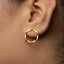 A close-up view of a person's ear wearing a gold-colored geometric earring.