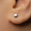 A close-up of a person's ear with a small silver earring featuring a smiley face design.