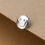 A silver smiley face button is resting on a beige surface.