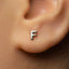 A close-up of a person's ear with a small silver earring featuring the letter "F" in the center.