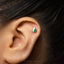 A close-up of a person's ear with a small, green and white earring in the earlobe.