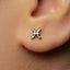 A close-up of a person's ear with a small silver earring featuring a zodiac symbol in the earlobe.