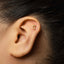 A close-up of a person's ear with a small gold earring featuring a crescent moon design.
