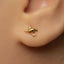 A close-up view of a person's ear adorned with a small gold earring featuring a shark design.