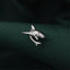 A silver shark pin is resting on a dark green fabric.