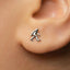 A close-up of a person's ear with a small silver earring featuring a figure of a person.