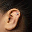 A person's ear with a small silver charm in the shape of a zodiac sign, specifically Capricorn, attached to the earlobe.
