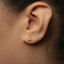 A close-up of a person's ear with a small gold earring featuring a zodiac symbol.