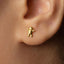 A close-up of a person's ear wearing a small gold-colored earring with a small figure on it.