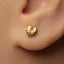 A close-up view of a person's ear adorned with a small gold earring featuring a leaf design.