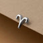 A silver earring in the shape of a zodiac sign, specifically a Leo, is resting on a brown surface.