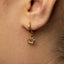 A close-up view of a person's ear wearing a gold-colored earring with a sun-shaped charm hanging from it.