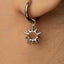 A close-up view of a person's ear wearing a silver earring with a sun-shaped charm hanging from it.