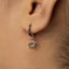 A close-up view of a person's ear wearing a silver earring with a sun-shaped charm hanging from it.