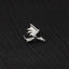 A small silver dragon pin is resting on a dark fabric surface.