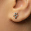 A close-up of a person's ear with a small, silver earring featuring a floral design.