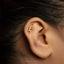 A close-up of a person's ear with a gold earring featuring a decorative leaf design.
