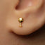 A close-up of a person's ear wearing a small gold earring shaped like a wine glass.