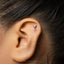 A close-up of a person's ear with a small silver earring in the shape of a wine glass.