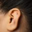 A close-up of a person's ear with a small gold number 3 stud in the earlobe.