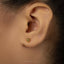 A close-up of a person's ear with a small gold earring featuring a cat's head design.