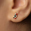 A close-up view of a person's ear adorned with a small, colorful earring featuring a bird design.
