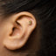 A close-up of a person's ear with a small gold earring in the earlobe.