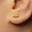 A close-up of a person's ear with a small gold earring in the earlobe.