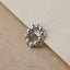 A silver ring with a circular design of small, shiny beads is resting on a textured surface.