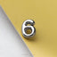 A close-up image of a shiny metal number 6 on a yellow background.