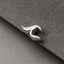 A close-up black and white image of a silver earring or ear cuff resting on a textured gray surface.