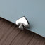 A silver-colored spade-shaped object is resting on a textured surface, such as a piece of fabric or a paper.