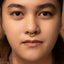A close-up portrait of a woman with a gold nose ring, looking directly at the camera with a neutral expression.