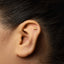 A close-up of a person's ear with a small gold-colored triangle-shaped earring in the earlobe.