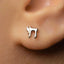 A close-up of a person's ear with a small silver earring featuring a Hebrew letter, likely the letter "S" or "S," attached to it.