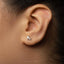 A close-up of a person's ear with a small silver earring featuring a skating shoe design.