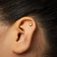 A close-up of a person's ear with a small gold earring in the earlobe.