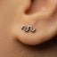 A close-up view of a person's ear with a small silver earring featuring a snake-like design.