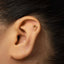 A close-up of a person's ear with a small gold-colored earring in the earlobe.