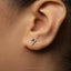 A close-up of a person's ear with a small silver triangle-shaped earring.