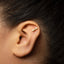 A close-up of a person's ear with a gold-colored earring in the earlobe.