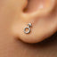 A close-up of a person's ear with a small silver earring featuring a male symbol, likely a symbol of gender identity or expression.