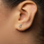 A close-up of a person's ear with a small silver earring featuring a male symbol, likely a symbol of gender identity or expression.