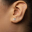 A close-up of a person's ear with a small, square-shaped earring in the earlobe.