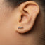 A close-up of a person's ear with a small, silver earring in the earlobe.