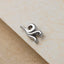 A silver-colored metal charm or pendant is resting on a textured surface, such as a piece of paper or a fabric.