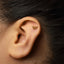 A close-up of a person's ear with a small gold earring in the earlobe.