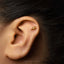 A close-up of a person's ear with a small gold earring in the earlobe.