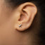 A close-up of a person's ear with a small silver bird earring in the earlobe.